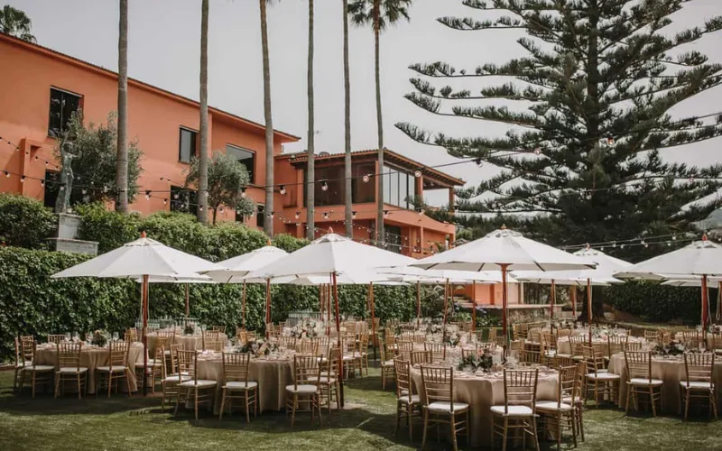 Round tables under white parasols beside a terracotta hacienda