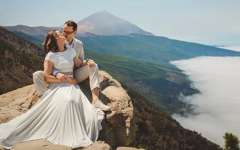 Couple seated on a rock above the clouds with Mount Teide behind