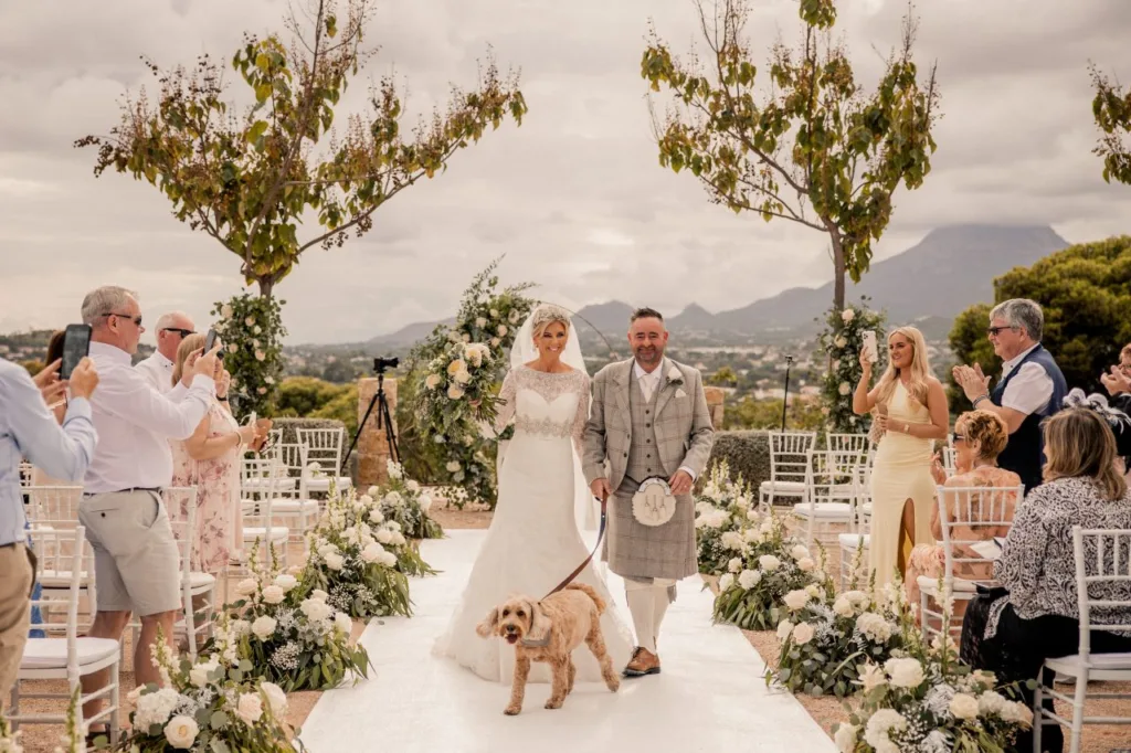 bride and groom walking down a wedding isle in spain with mountains in the background