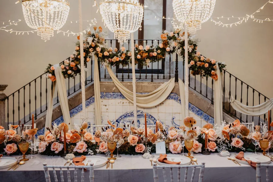 Top table beneath chandeliers with a full floral runner and draping