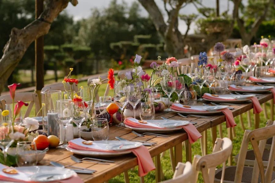 Long table set with mixed flowers beneath olive trees