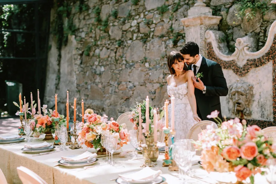 Couple at a table set with peach flowers and candles against a stone wall