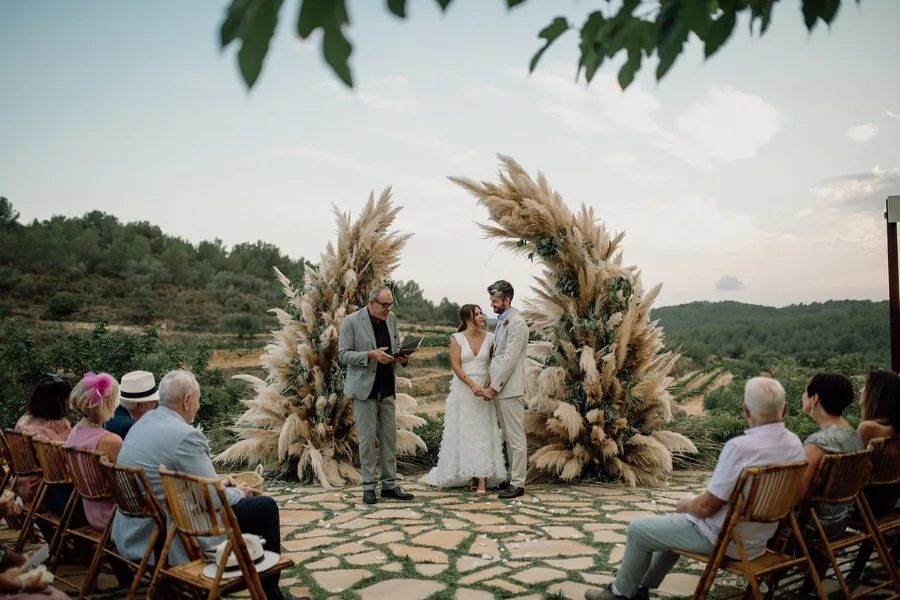Outdoor ceremony beneath a pampas grass arch with guests seated